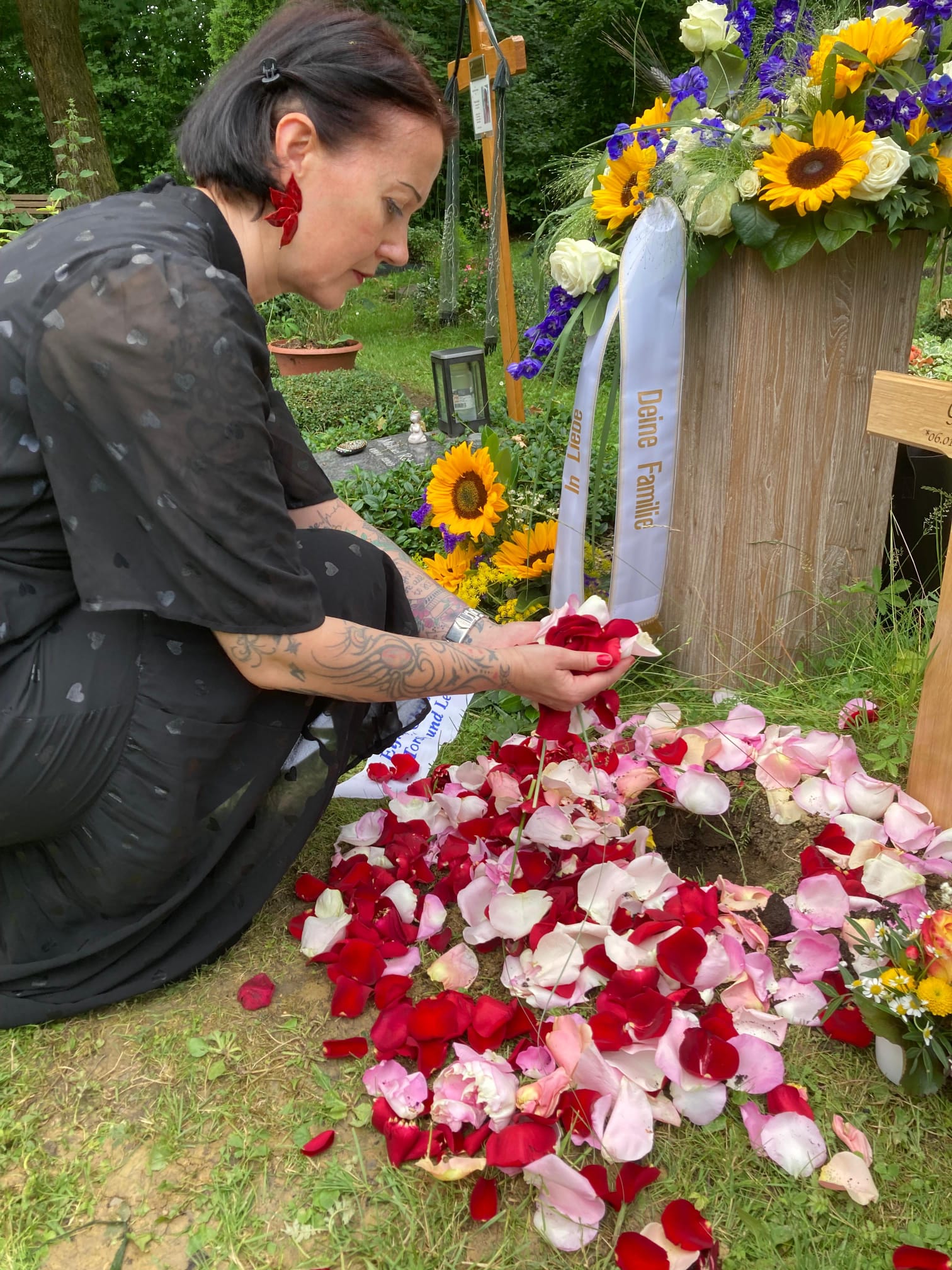 Frau Brauneis streut Rosenblätter auf ein Grab mit Blumen und Sonnenblumen