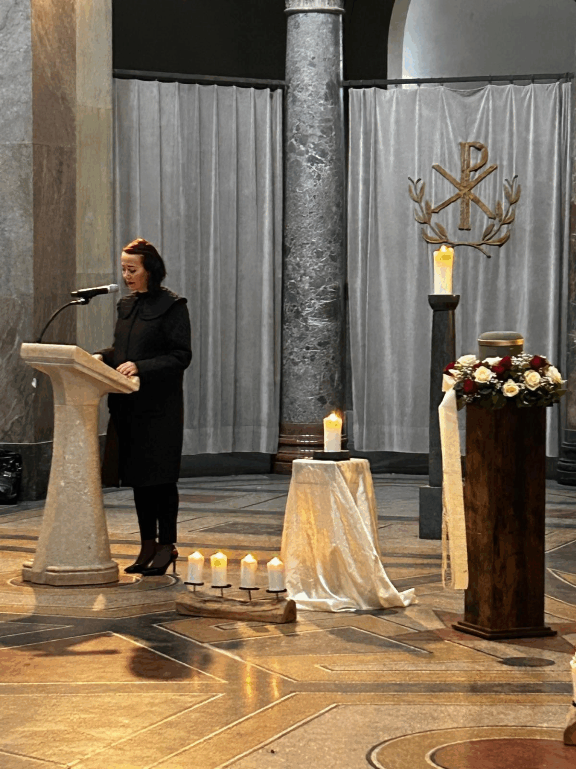 Frau Brauneis hält eine Trauerrede am Rednerpult vor einer Urne mit Blumenschmuck