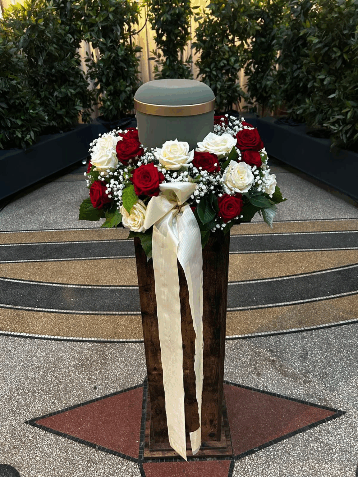 Urne mit Blumen- und Rosenschmuck auf einem Sockel